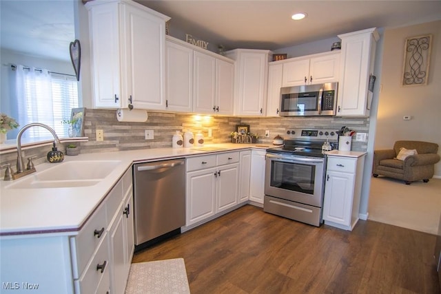 kitchen with appliances with stainless steel finishes, dark wood-type flooring, decorative backsplash, white cabinets, and sink