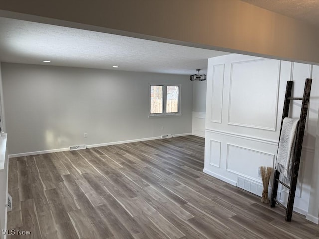 unfurnished living room with a textured ceiling, a notable chandelier, and dark wood-type flooring