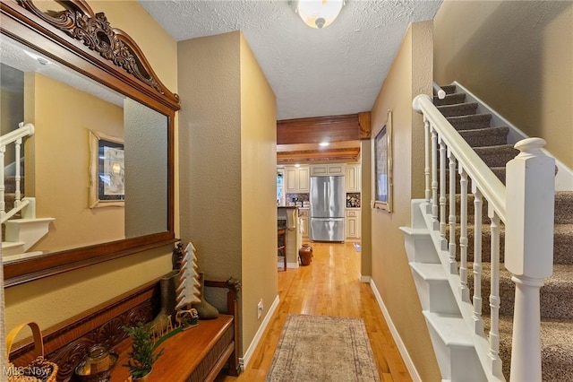 hallway featuring a textured ceiling, stairway, light wood-style flooring, and baseboards