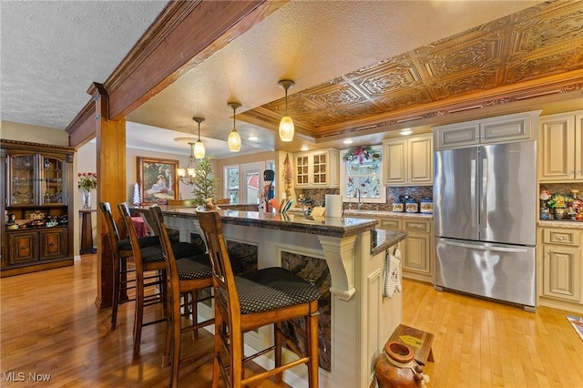 kitchen featuring an ornate ceiling, a breakfast bar, freestanding refrigerator, cream cabinets, and a sink