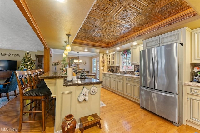 kitchen with an ornate ceiling, decorative backsplash, an inviting chandelier, light wood-style floors, and freestanding refrigerator