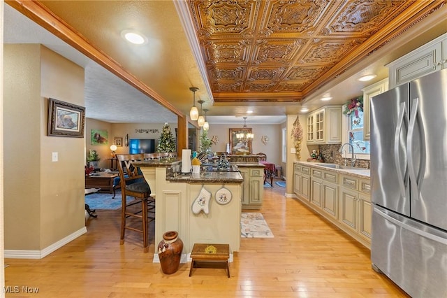 kitchen featuring cream cabinetry, freestanding refrigerator, a tray ceiling, a kitchen bar, and an ornate ceiling