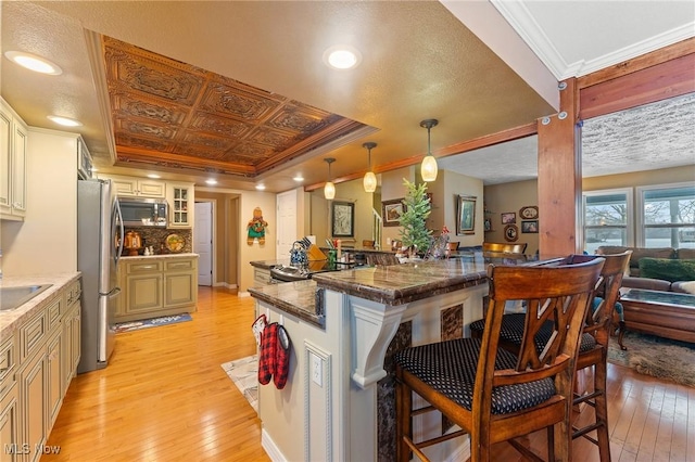 kitchen featuring a tray ceiling, stainless steel appliances, light wood-style floors, ornamental molding, and a kitchen breakfast bar