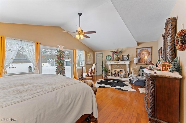 bedroom with a ceiling fan, a glass covered fireplace, lofted ceiling, hardwood / wood-style flooring, and access to outside