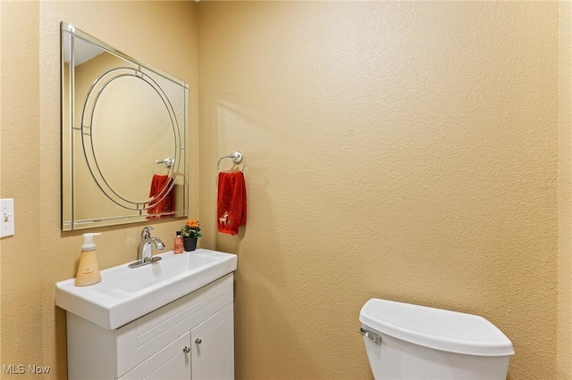 bathroom featuring toilet, a textured wall, and vanity