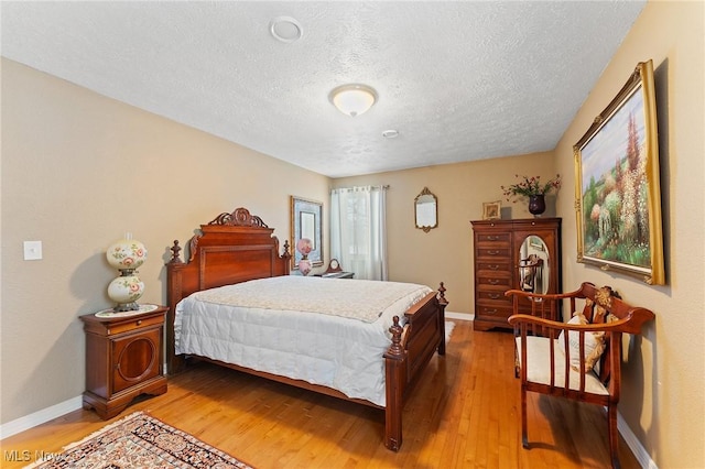 bedroom featuring light wood-type flooring, a textured ceiling, and baseboards