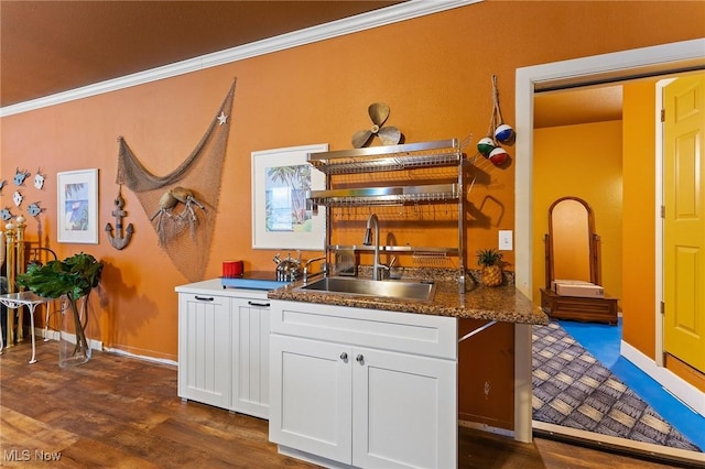 kitchen featuring baseboards, dark wood finished floors, crown molding, white cabinetry, and a sink