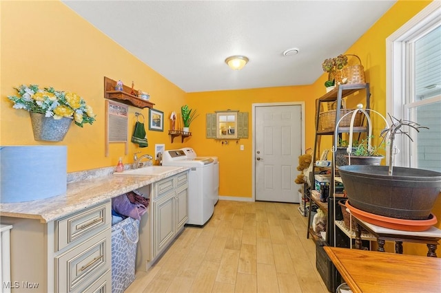 washroom with light wood finished floors, cabinet space, a sink, separate washer and dryer, and baseboards