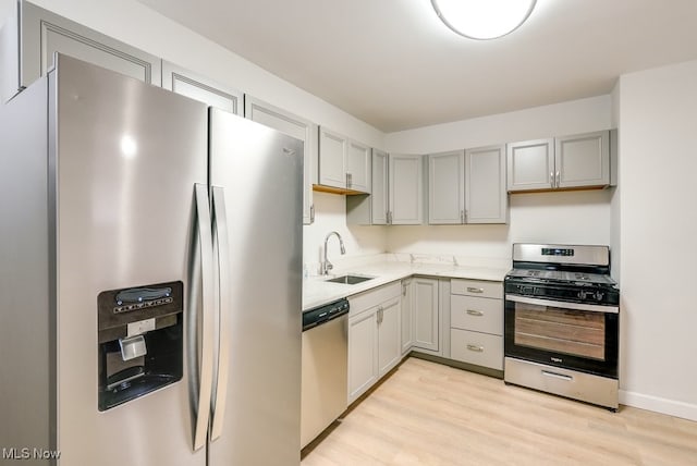 kitchen with appliances with stainless steel finishes, light hardwood / wood-style floors, gray cabinets, and sink