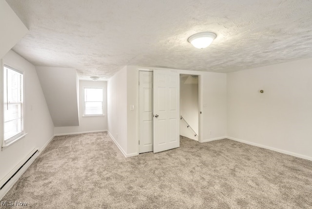 additional living space with a textured ceiling, baseboard heating, vaulted ceiling, and light colored carpet