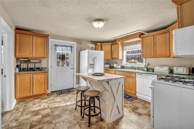 kitchen featuring white appliances, a textured ceiling, a center island, a kitchen bar, and sink