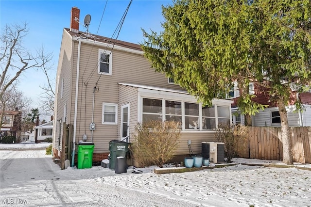 snow covered back of property featuring central AC and a sunroom