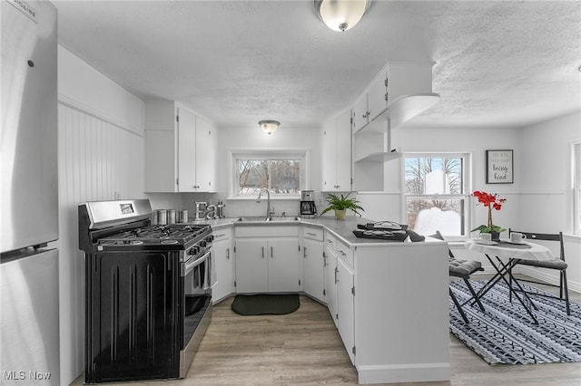 kitchen with a textured ceiling, stainless steel appliances, light hardwood / wood-style floors, white cabinets, and sink