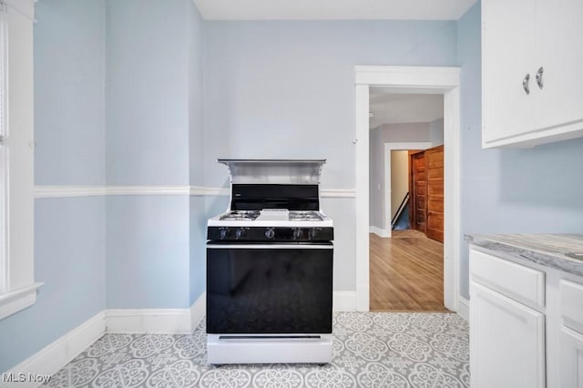 kitchen featuring range with gas stovetop, light tile patterned floors, white cabinets, and light stone countertops