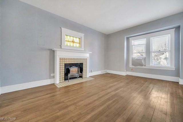 unfurnished living room featuring a tiled fireplace, a wealth of natural light, and hardwood / wood-style flooring