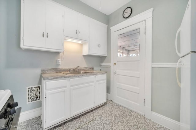 kitchen with light tile patterned floors, stainless steel range, white cabinetry, white refrigerator, and sink