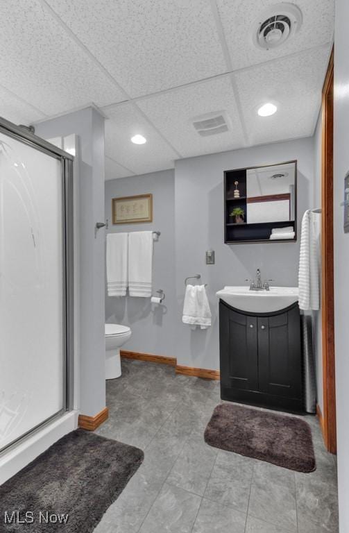 bathroom featuring vanity, a shower with door, toilet, and a drop ceiling