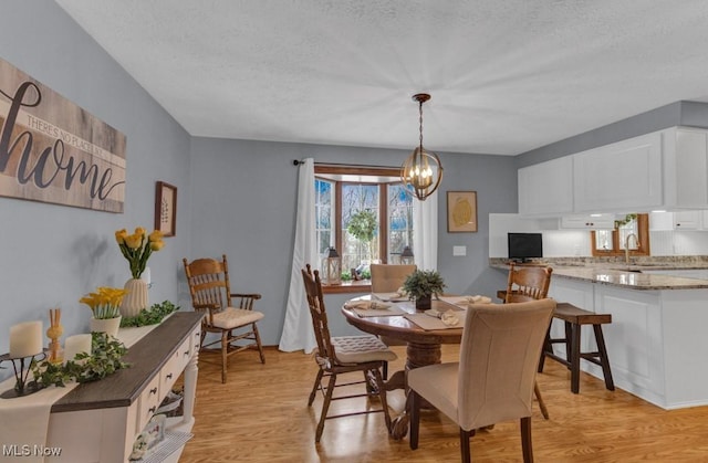 dining room with sink, a chandelier, a textured ceiling, and light hardwood / wood-style floors