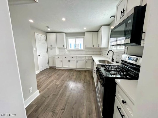 kitchen featuring sink, white cabinetry, gas range oven, hardwood / wood-style flooring, and decorative backsplash