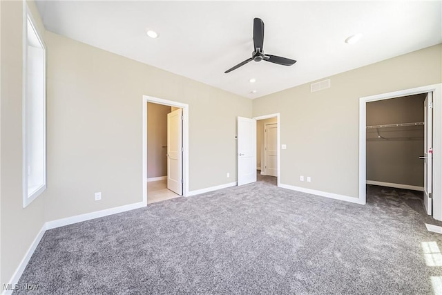 unfurnished bedroom with a walk in closet, light carpet, a closet, and ceiling fan