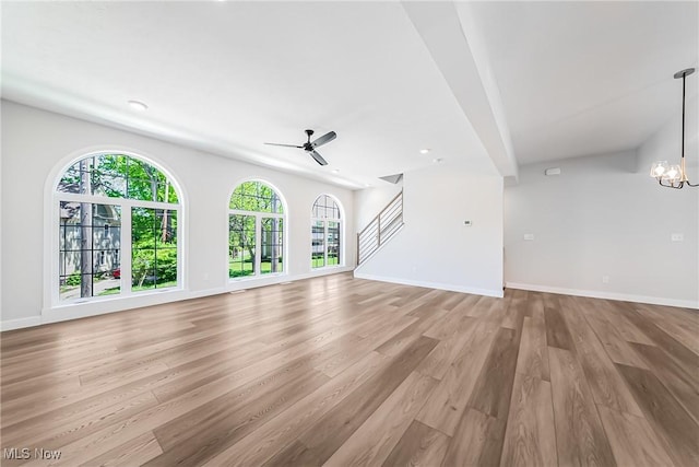 unfurnished living room with ceiling fan with notable chandelier, a healthy amount of sunlight, and light hardwood / wood-style flooring