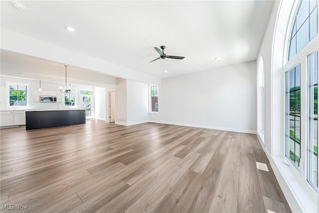 unfurnished living room featuring ceiling fan with notable chandelier and light wood-type flooring