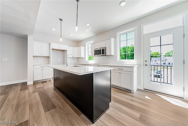 kitchen featuring white cabinetry, an island with sink, sink, light hardwood / wood-style flooring, and decorative light fixtures