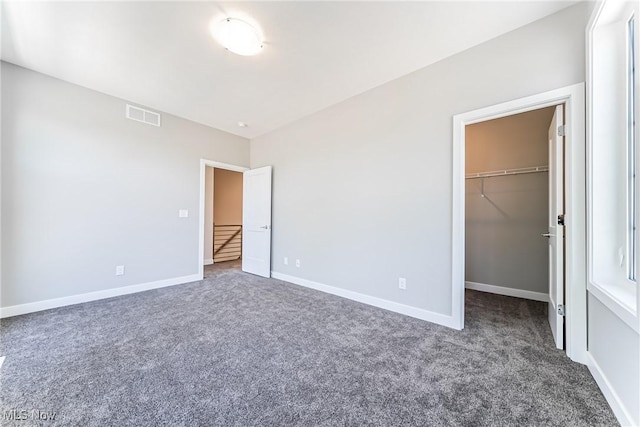 unfurnished bedroom featuring dark colored carpet, a closet, and a spacious closet