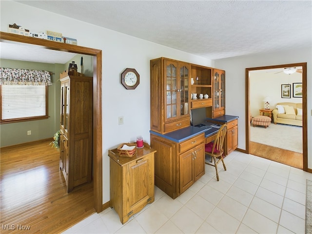 home office with a textured ceiling, ceiling fan, light hardwood / wood-style floors, and built in desk