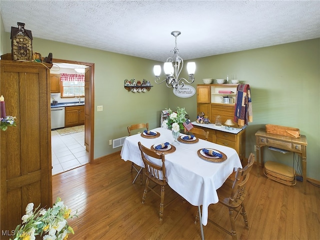 dining area featuring a textured ceiling, light wood-type flooring, an inviting chandelier, and sink