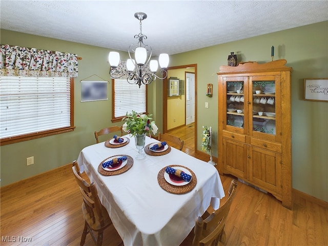 dining space featuring a textured ceiling, light wood-type flooring, and a notable chandelier