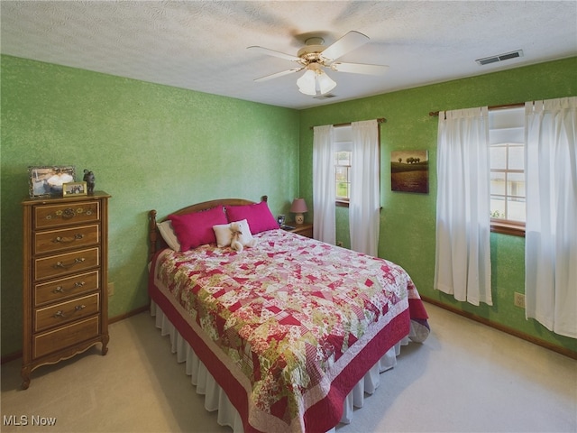 bedroom with light colored carpet, ceiling fan, and a textured ceiling