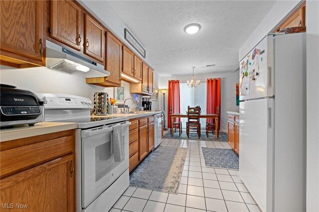 kitchen featuring white appliances, a textured ceiling, a chandelier, decorative light fixtures, and light tile patterned floors