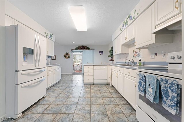 kitchen featuring white appliances, kitchen peninsula, a textured ceiling, white cabinets, and backsplash