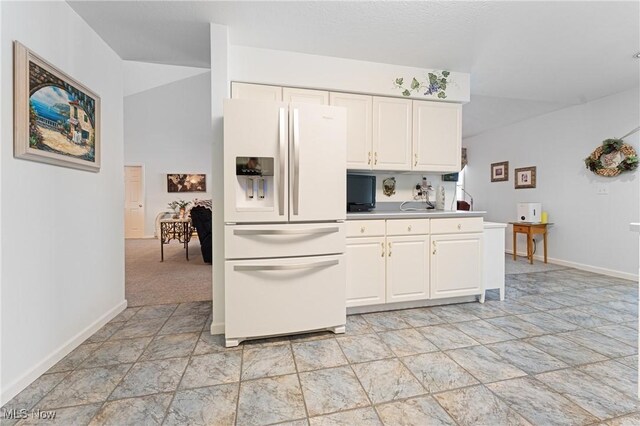 kitchen featuring white cabinets, white refrigerator with ice dispenser, and light carpet