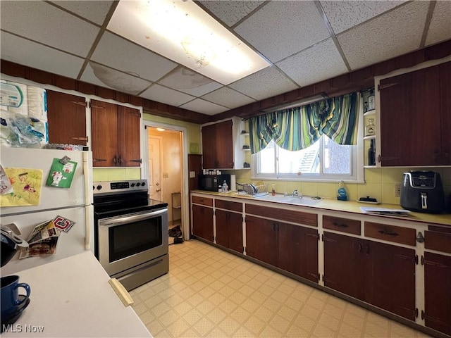 kitchen featuring stainless steel electric stove, white refrigerator, a drop ceiling, dark brown cabinetry, and backsplash