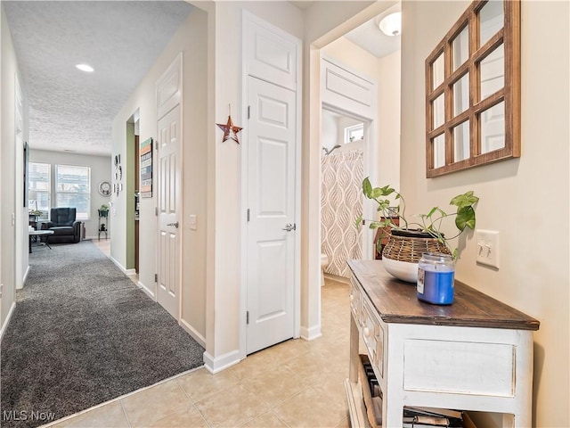 hallway featuring light colored carpet and a textured ceiling