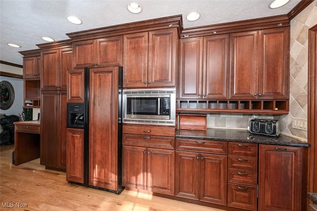 kitchen with dark stone counters, built in appliances, tasteful backsplash, ornamental molding, and light hardwood / wood-style flooring