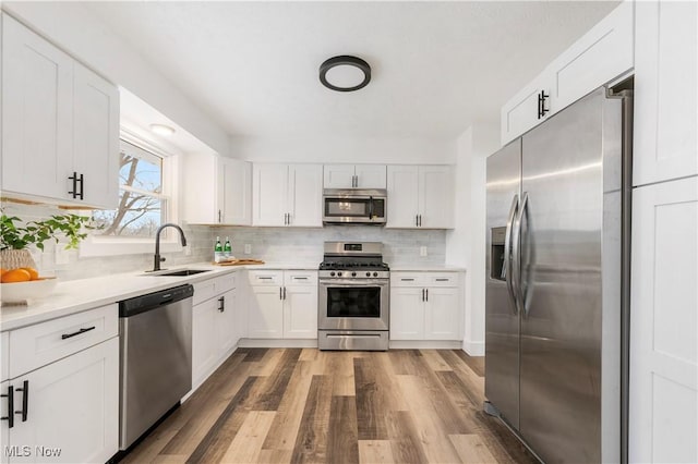 kitchen with stainless steel appliances, sink, white cabinetry, tasteful backsplash, and light hardwood / wood-style flooring