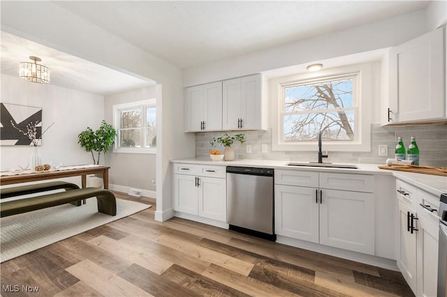 kitchen with white cabinets, light wood-type flooring, sink, stainless steel dishwasher, and tasteful backsplash