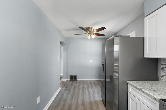 kitchen featuring light stone countertops, light hardwood / wood-style floors, stainless steel refrigerator with ice dispenser, white cabinets, and ceiling fan