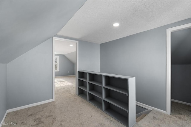 additional living space featuring a textured ceiling, light colored carpet, and vaulted ceiling