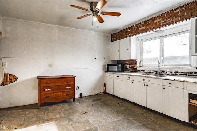 kitchen with sink, white cabinets, ceiling fan, tasteful backsplash, and brick wall