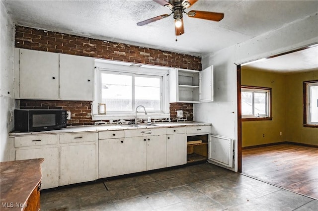 kitchen with brick wall, ceiling fan, a textured ceiling, sink, and white cabinetry