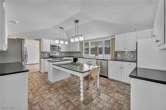 kitchen with pendant lighting, white cabinets, lofted ceiling, stainless steel appliances, and backsplash