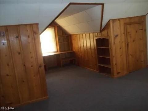 bonus room with wood walls, vaulted ceiling, and dark colored carpet