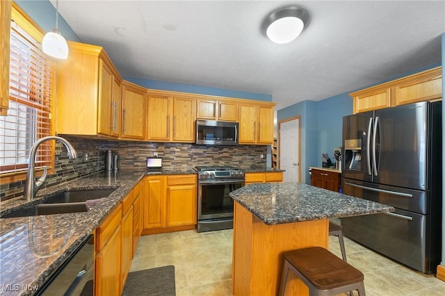 kitchen featuring stainless steel appliances, a center island, dark stone countertops, and sink