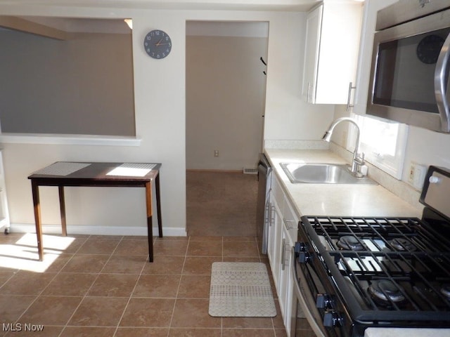 kitchen with appliances with stainless steel finishes, white cabinets, tile patterned floors, and sink