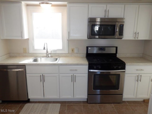 kitchen with appliances with stainless steel finishes, white cabinets, dark tile patterned floors, and sink