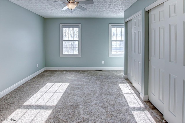 unfurnished bedroom with multiple windows, ceiling fan, light carpet, and multiple closets